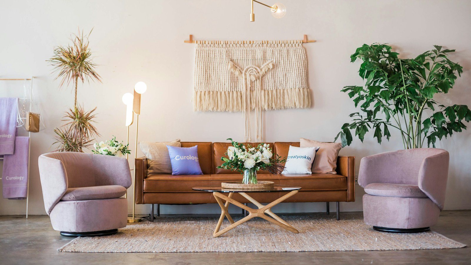 A living room styled with plants, cushions and a macramé wall hanging